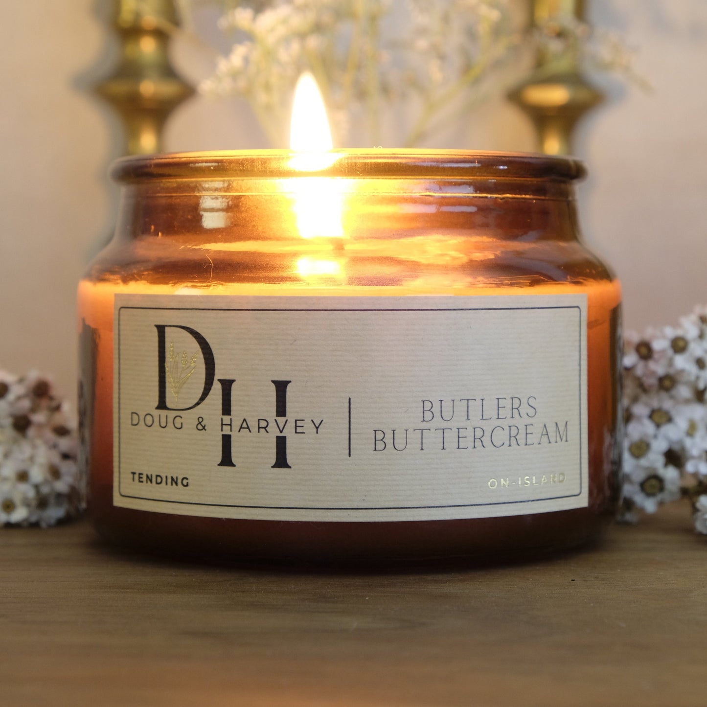 Doug & Harvey Butlers Buttercream candle glowing in amber glass jar, styled with native florals and vintage brass candlesticks — Tasmanian-made home fragrance inspired by rural charm and slow living