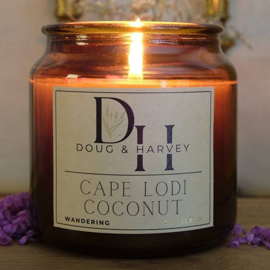 Candle in a glass jar labeled 'Doug & Harver Cape Lodi Coconut' with a blurred background.