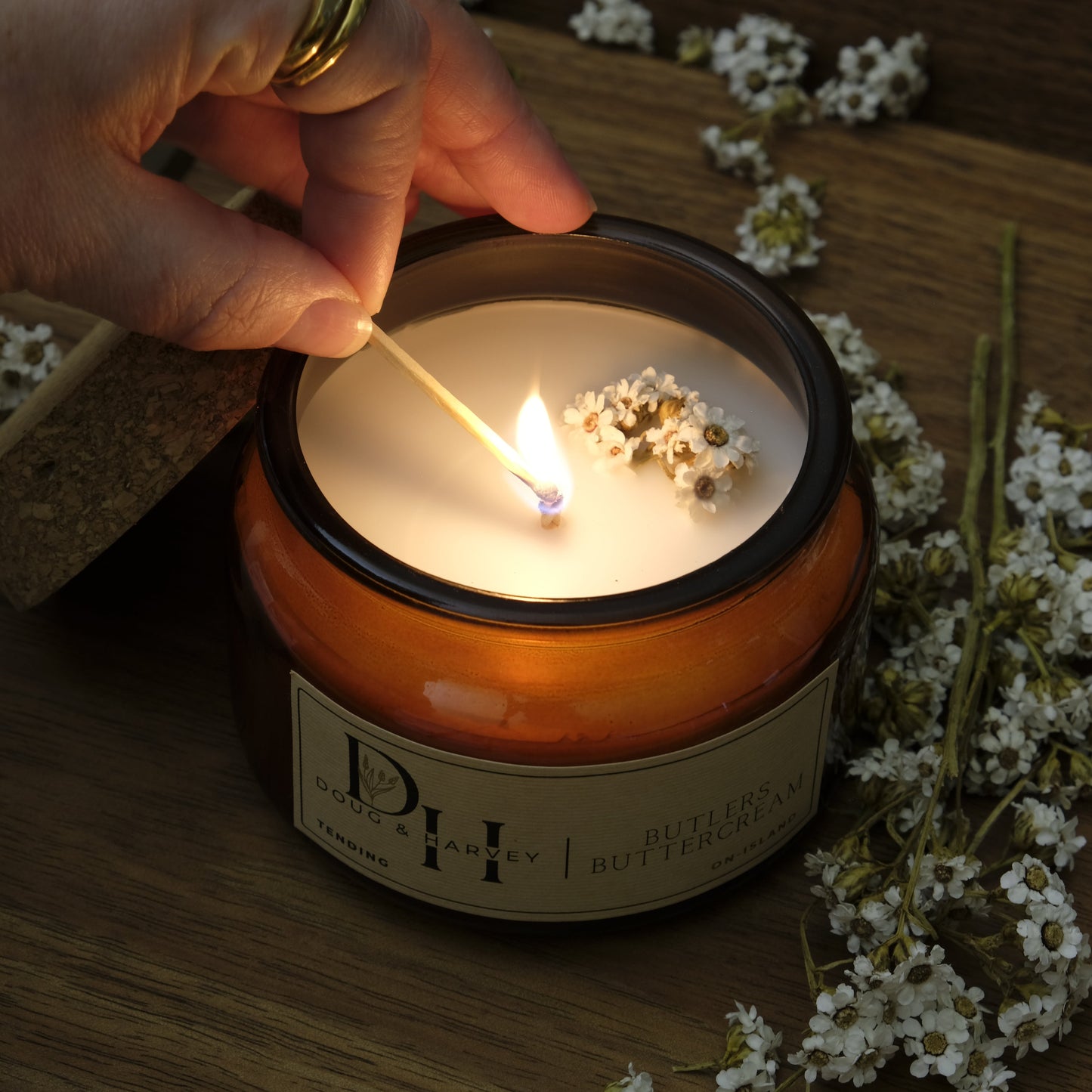 Hand lighting a candle in a decorative container with flowers on a wooden surface