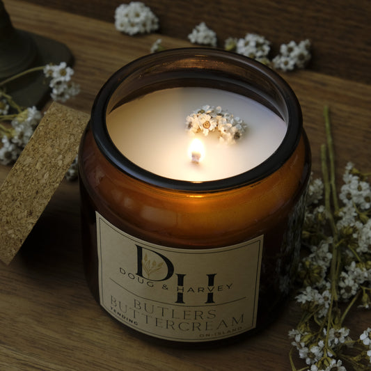 Candle in a glass jar with a label, surrounded by small white flowers on a wooden surface