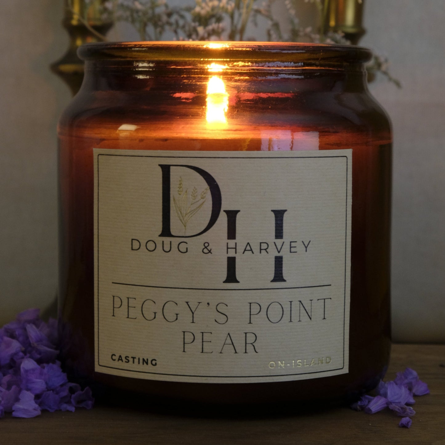 Candle in a brown jar with a label reading 'Doug & Harvey Peggy's Point Pear' on a wooden surface.