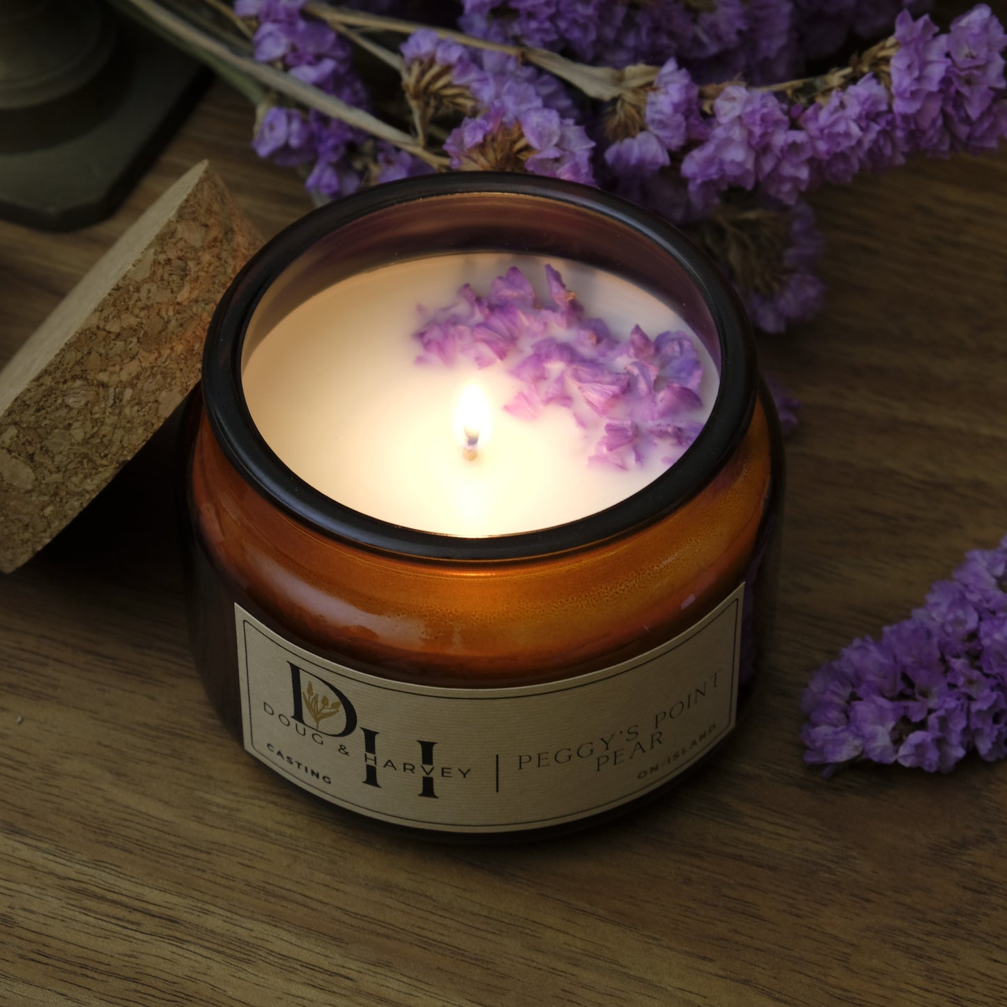 Candle with a lavender design on the lid, surrounded by lavender flowers on a wooden surface.
