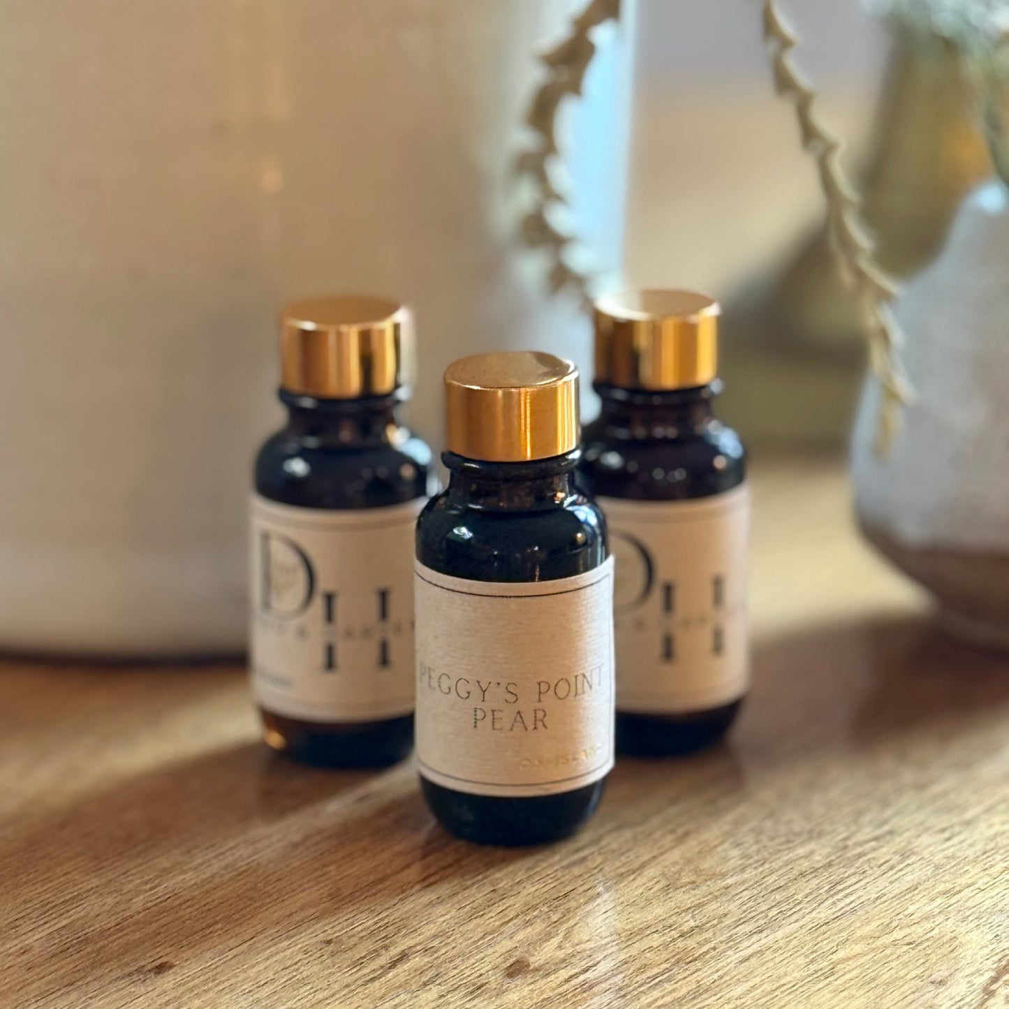 Three small bottles with gold caps on a wooden surface, with a blurred decorative background.