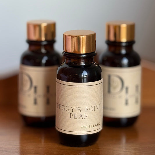 Three bottles of 'Peggy's Point Pear' on a wooden surface with a neutral background diffuser oil