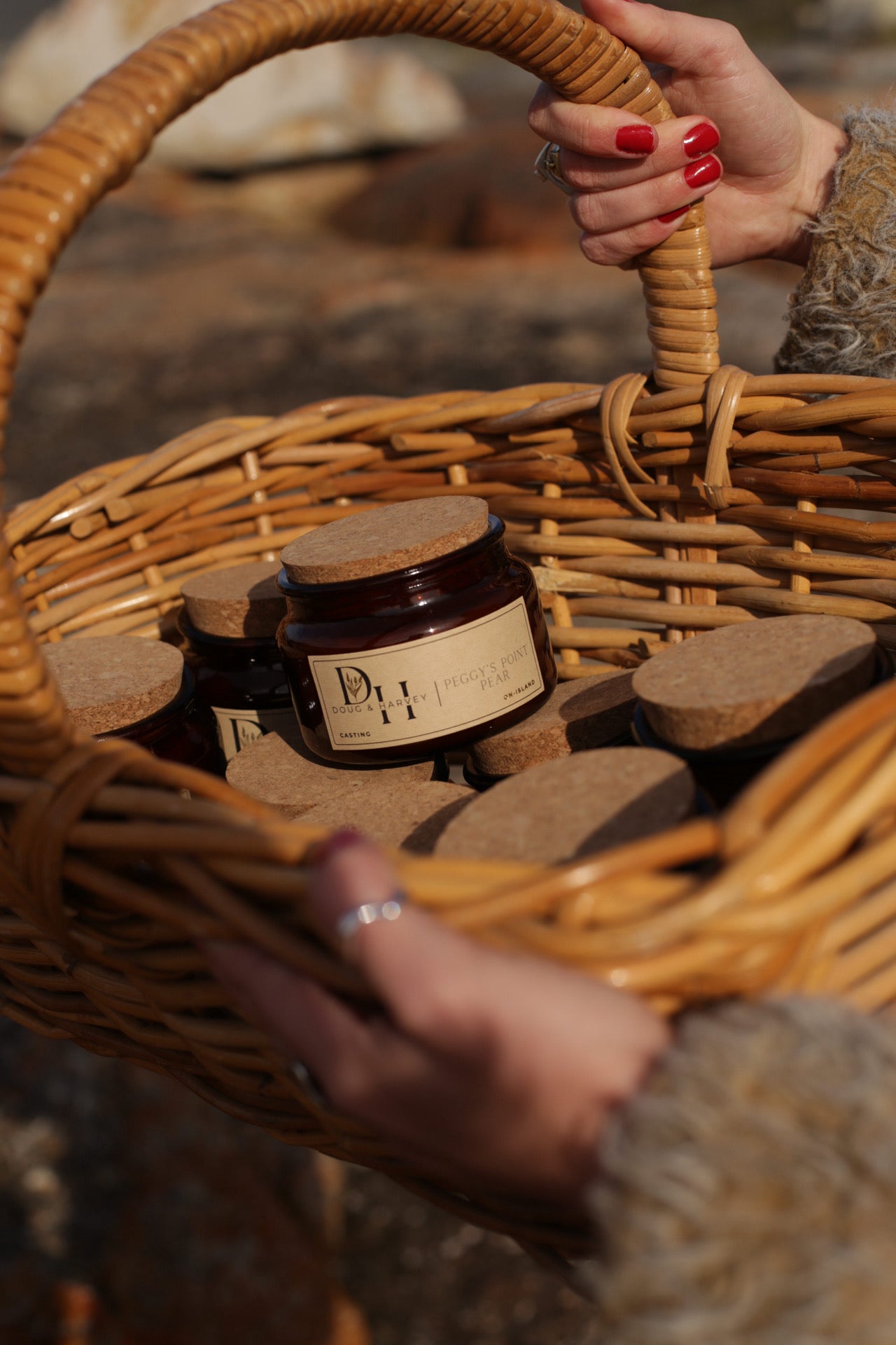 Basket of Doug & Harvey candles in amber glass jars with cork lids, featuring Peggy’s Point Pear candle at the front, carried outdoors by hand with natural light.