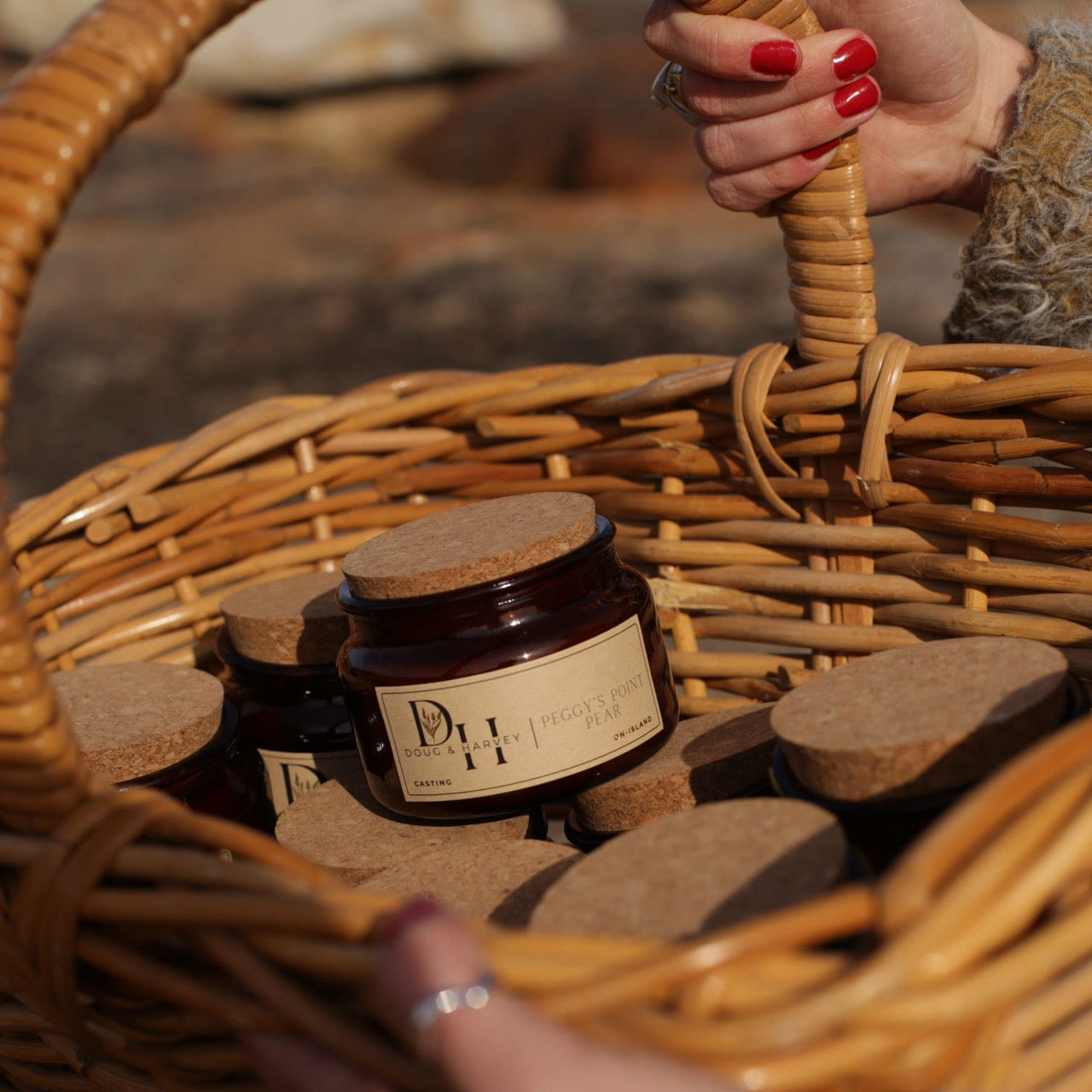 Basket of Doug & Harvey candles in amber glass jars with cork lids, featuring Peggy’s Point Pear candle at the front, carried outdoors by hand with natural light.