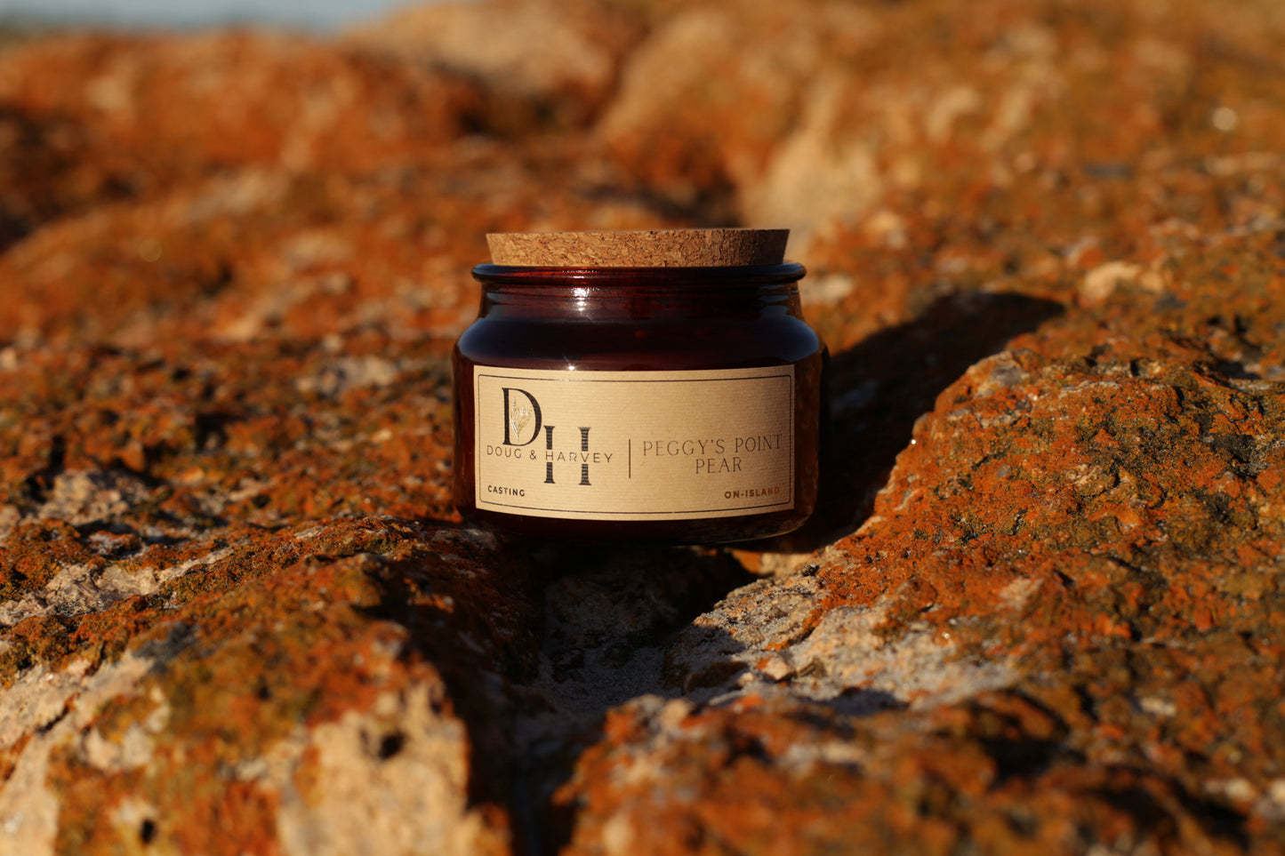 Doug & Harvey ‘Peggy’s Point Pear’ candle in an amber glass jar with cork lid, styled outdoors on textured Tasmanian rocks, highlighting its natural and coastal-inspired design.