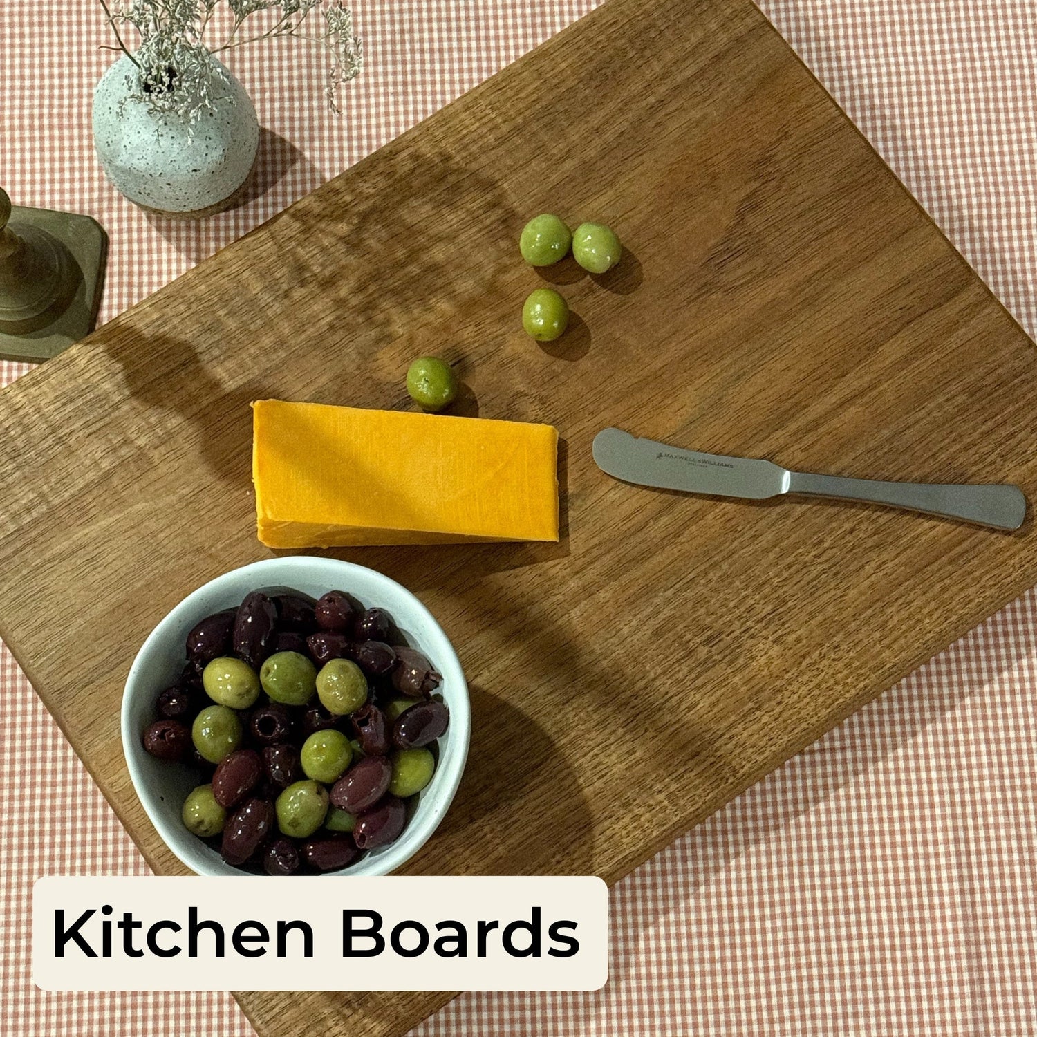 Doug & Harvey Tasmanian blackwood kitchen board collection cover image, styled with cheddar cheese, green and kalamata olives, and a cheese knife on a gingham tablecloth, with text overlay reading 'Kitchen Boards'.