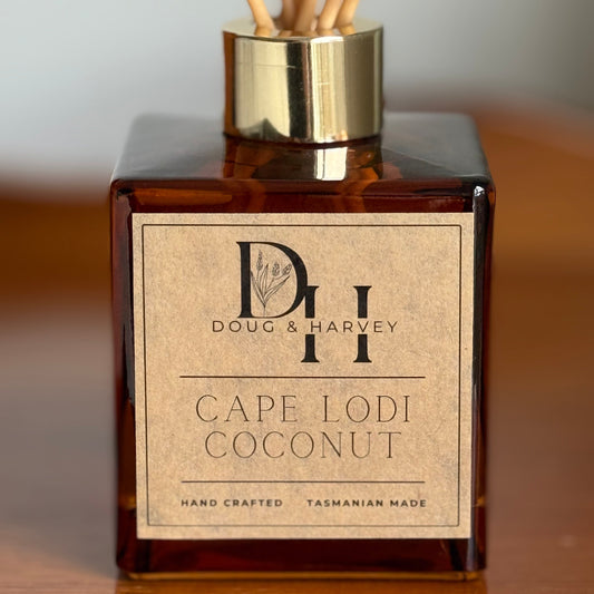 Reed diffuser bottle labeled 'Cape Lodi Coconut' by Doug & Harvey on a wooden surface.