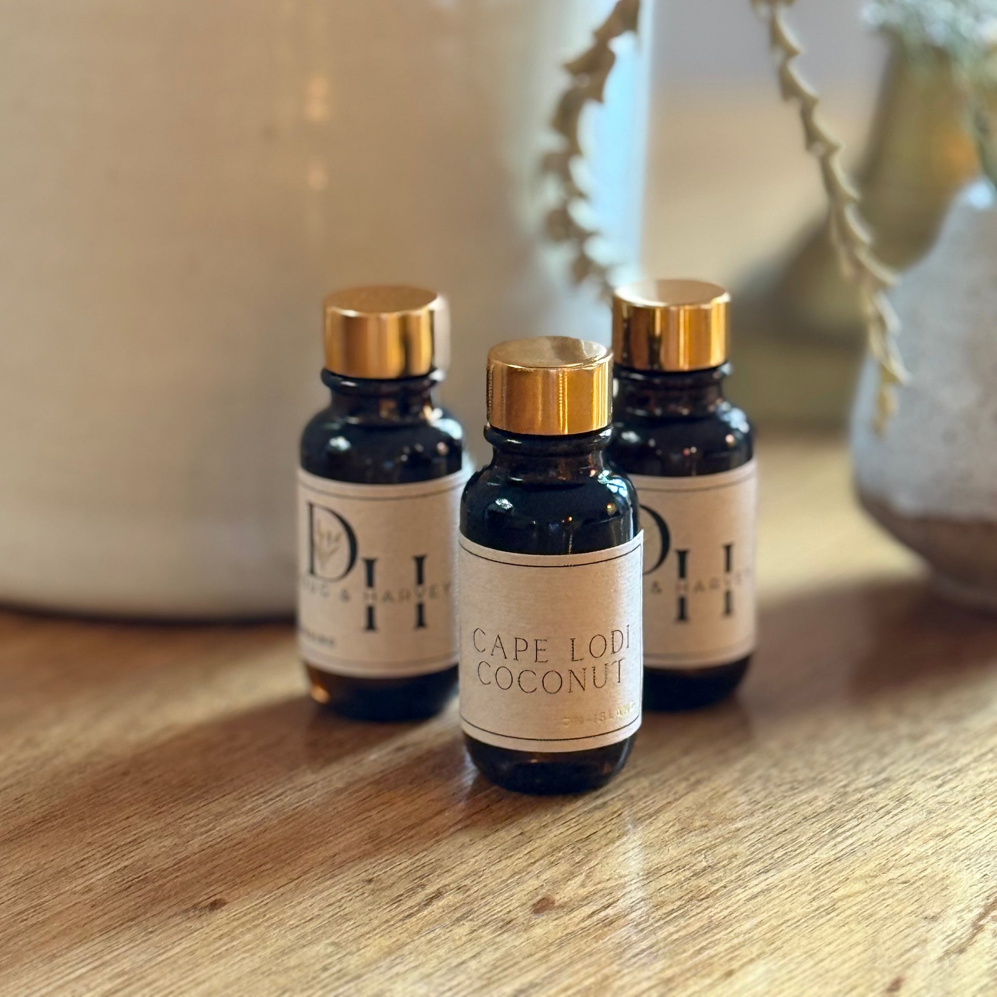 Three small bottles labeled 'Cape Loud Coconut' on a wooden surface with a blurred background.
