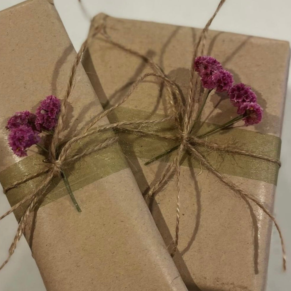 Two rectangular gifts wrapped in brown paper, tied with twine and adorned with dried flowers.