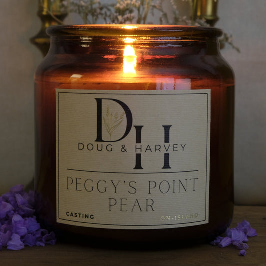 Candle in a brown jar with a label reading 'Doug & Harvey Peggy's Point Pear' on a wooden surface.