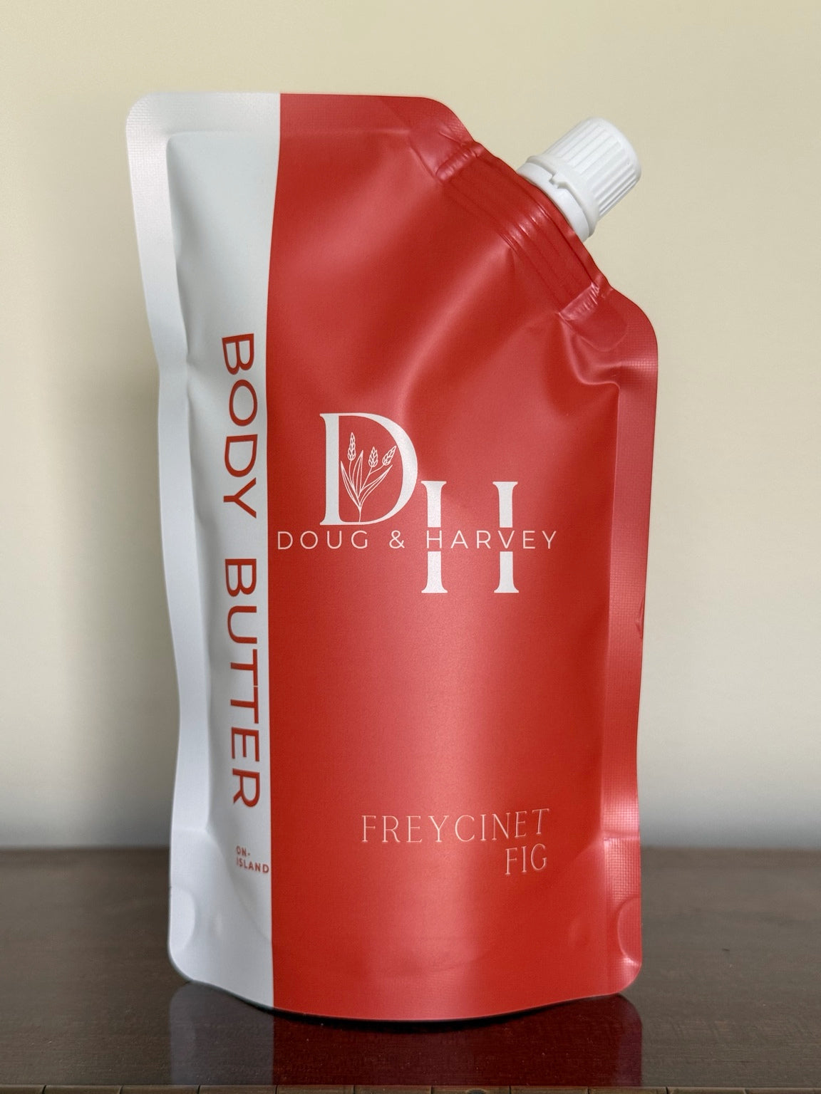 Front of the Doug & Harvey Freycinet Fig Body Butter coral-and-cream squeeze pouch with a white cap, standing on dark timber.
