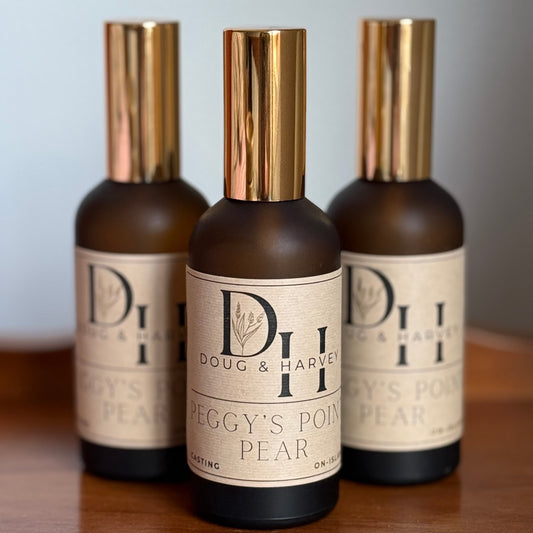 Three bottles of Doug & Harvey Peggy's Point Pear on a wooden surface with a light gray background.