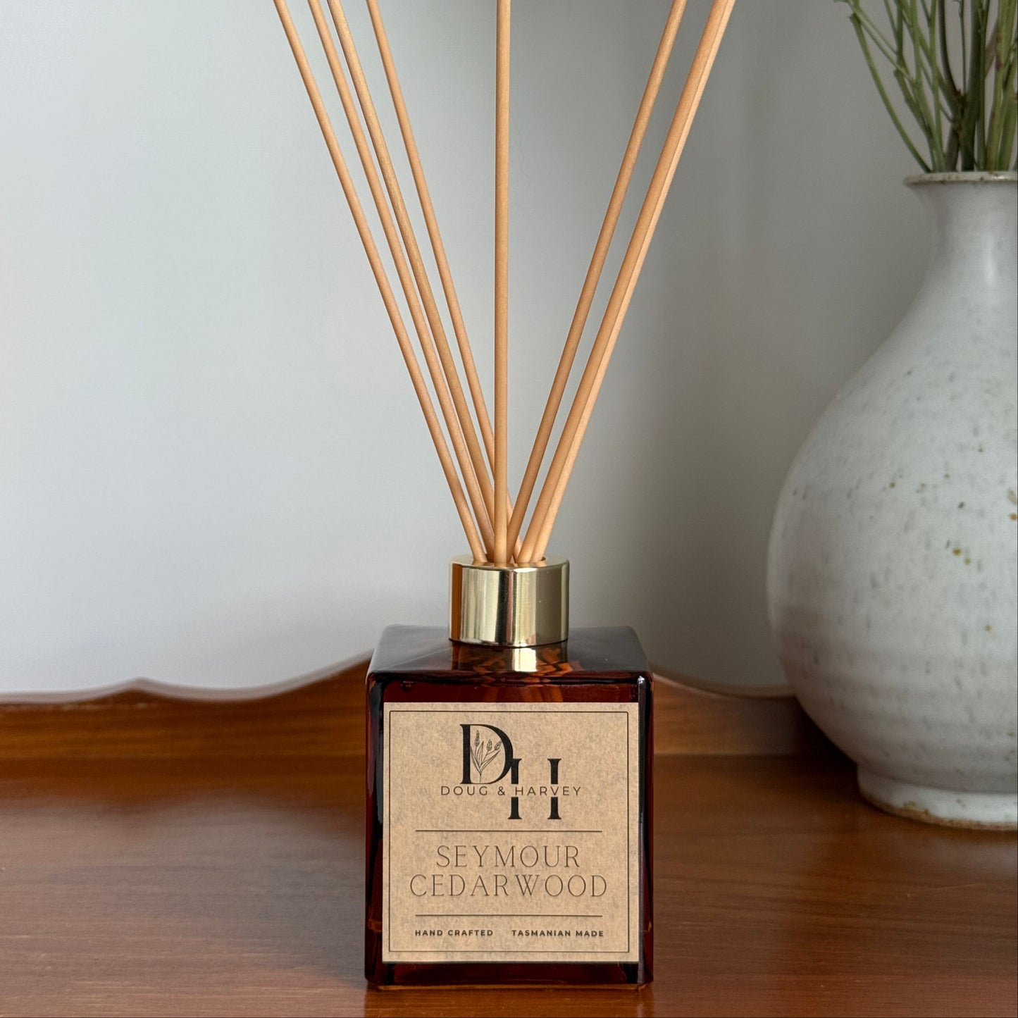Reed diffuser with wooden sticks on a white surface, featuring a brand label.