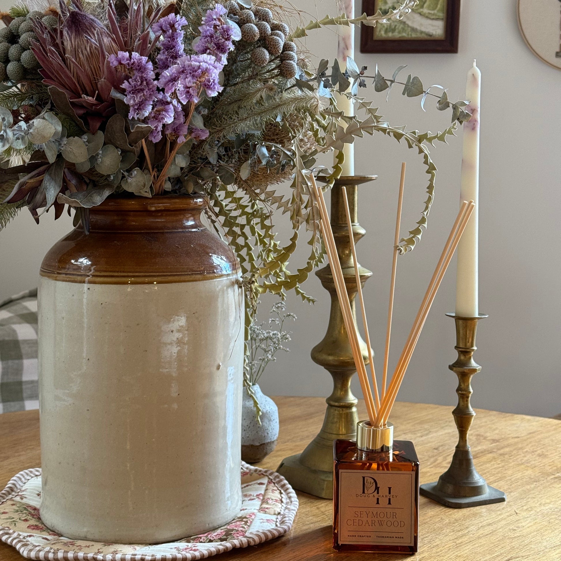 Decorative setup with a vase, flowers, and natural reed diffusers in cedarwood scent on a wooden surface.