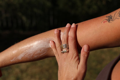 Close-up of Doug & Harvey body butter being massaged into a forearm outdoors in sunlight.