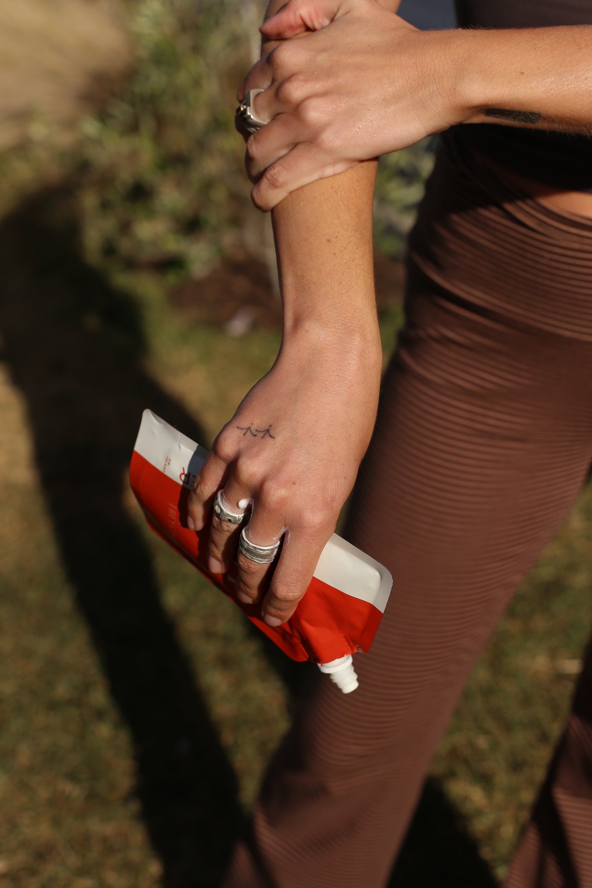 Person massaging Doug & Harvey body butter into their forearm outdoors while holding the orange and white pouch.