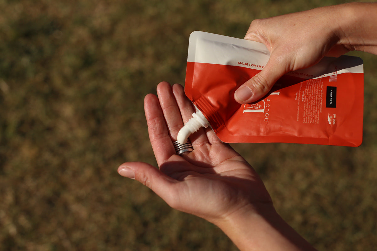 Doug & Harvey body butter being squeezed from an orange and white pouch into an open palm outdoors.
