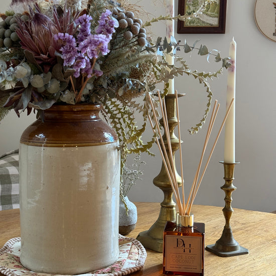 Cape Lodi Coconut Natural Reed Diffuser inserting rattan reeds into square diffuser on country table