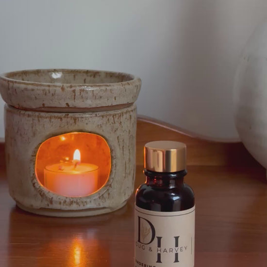 Diffuser oil being dispensed into diffuser oil burner with tea light candle burning on a wood surface