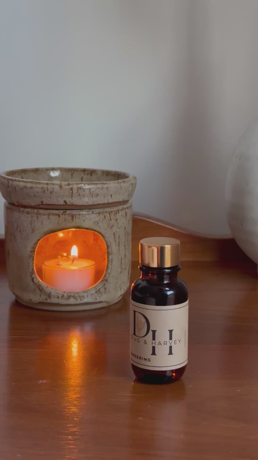 Diffuser oil being dispensed into diffuser oil burner with tea light candle burning on a wood surface